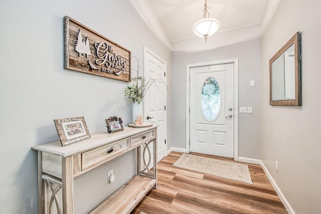 foyer featuring baseboards, light wood-style flooring, and lofted ceiling