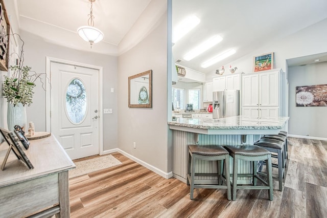 foyer featuring baseboards, light wood-style flooring, and lofted ceiling