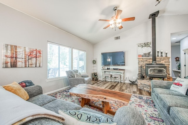 living area featuring visible vents, a wood stove, wood finished floors, baseboards, and a ceiling fan