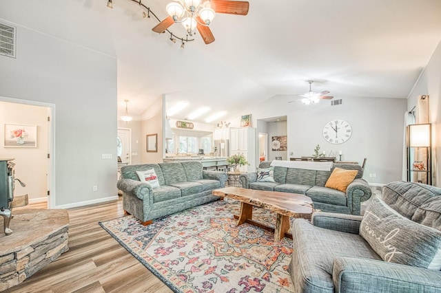 living room with a ceiling fan, visible vents, vaulted ceiling, baseboards, and light wood finished floors