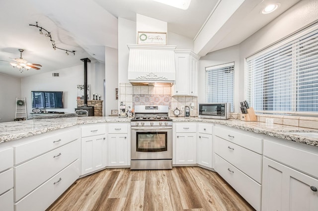 kitchen featuring stainless steel appliances, vaulted ceiling, decorative backsplash, and a wood stove