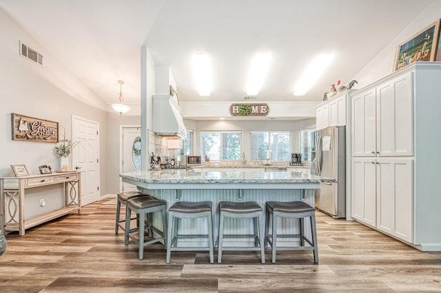 kitchen with a kitchen breakfast bar, visible vents, light stone counters, a peninsula, and stainless steel fridge