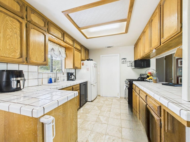 kitchen featuring black dishwasher, stainless steel gas range, tile countertops, a sink, and backsplash