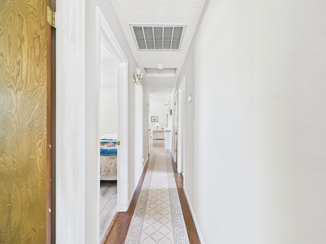 hall featuring a textured ceiling, baseboards, visible vents, and wood finished floors