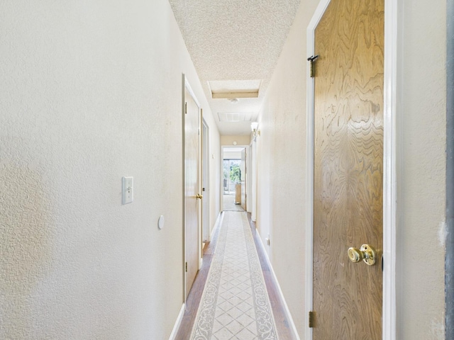 hall with attic access, a textured ceiling, light tile patterned floors, baseboards, and a textured wall