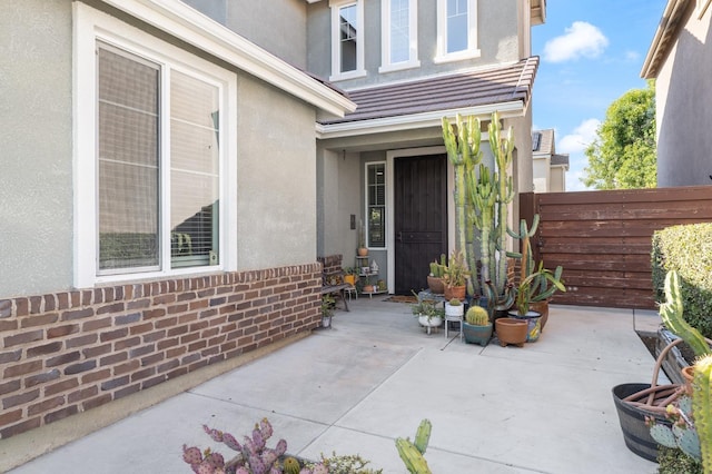 entrance to property with brick siding, a patio area, stucco siding, and fence