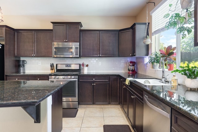 kitchen featuring decorative backsplash, light tile patterned flooring, dark brown cabinets, a sink, and appliances with stainless steel finishes