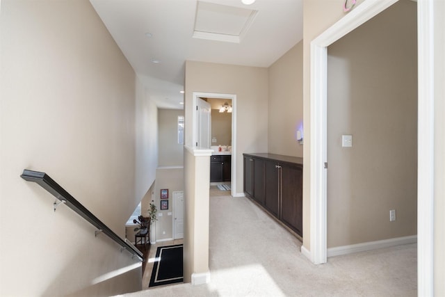 hallway featuring baseboards, light carpet, attic access, and an upstairs landing