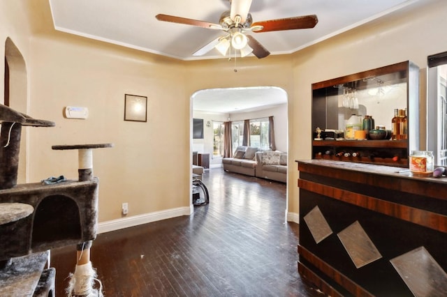 interior space featuring a ceiling fan, ornamental molding, baseboards, dark wood-type flooring, and arched walkways