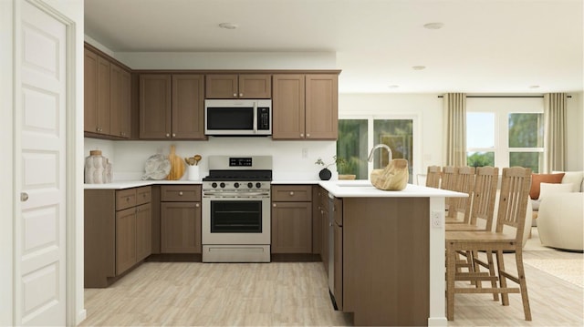 kitchen with a peninsula, light wood-style floors, a breakfast bar area, stainless steel range with gas cooktop, and light countertops