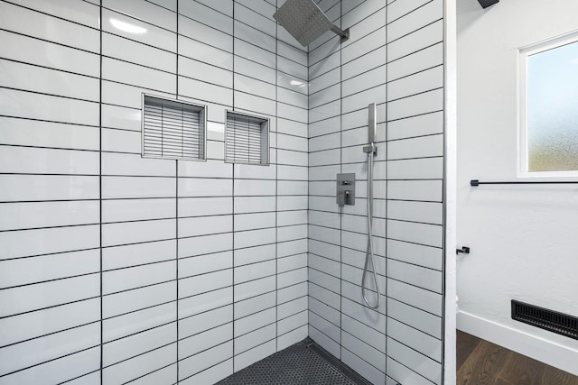 bathroom with baseboards, wood finished floors, and tiled shower