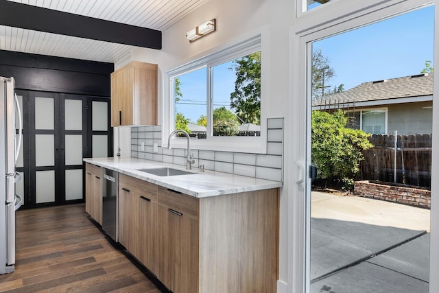 kitchen featuring decorative backsplash, light brown cabinetry, stainless steel dishwasher, a sink, and beamed ceiling