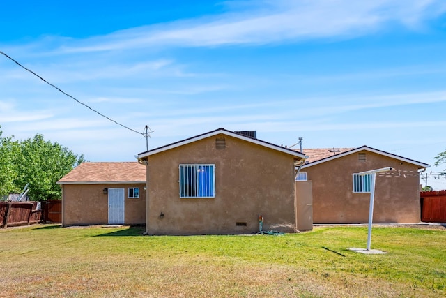 rear view of property featuring a lawn, fence, and stucco siding