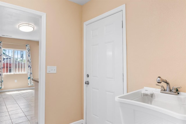 laundry area featuring baseboards, a sink, light tile patterned floors, and visible vents