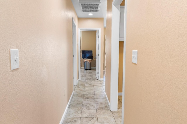 hall with a textured wall, visible vents, and baseboards