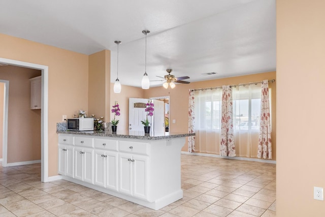 kitchen with a ceiling fan, visible vents, white microwave, a peninsula, and white cabinetry