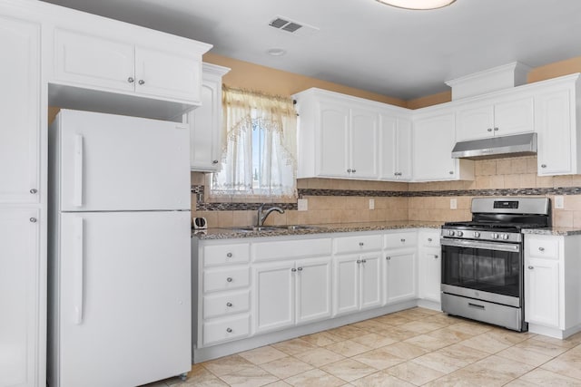 kitchen with stainless steel range with gas stovetop, light stone countertops, a sink, freestanding refrigerator, and under cabinet range hood