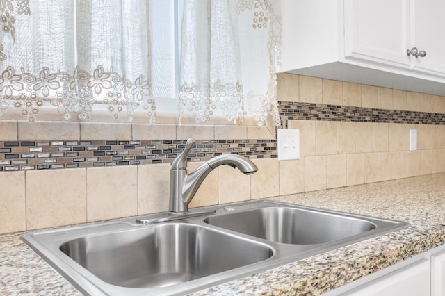 interior details with backsplash, white cabinets, and a sink