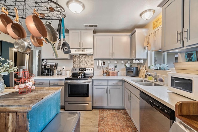 kitchen featuring visible vents, stainless steel appliances, a sink, light countertops, and under cabinet range hood