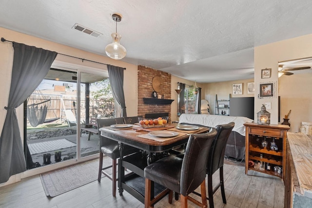 dining room with visible vents, a brick fireplace, a textured ceiling, a ceiling fan, and light wood finished floors