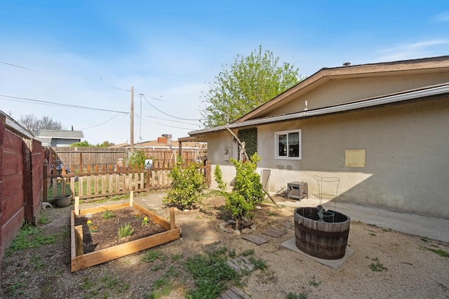 back of house with stucco siding, fence, and a vegetable garden