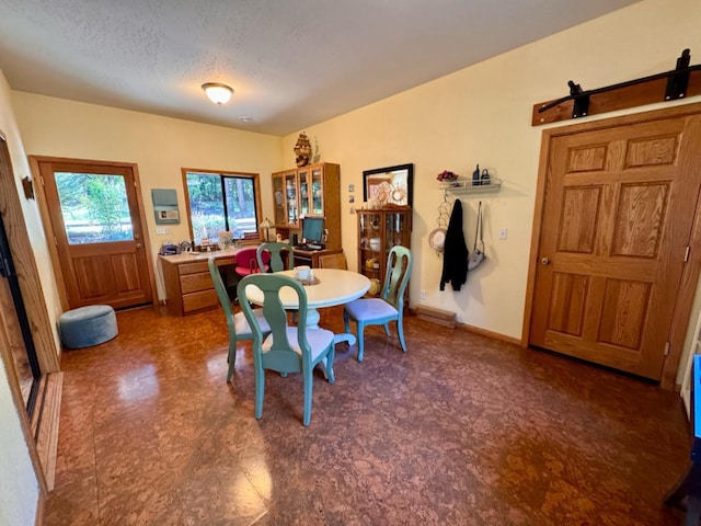 dining space featuring a textured ceiling, a barn door, and baseboards