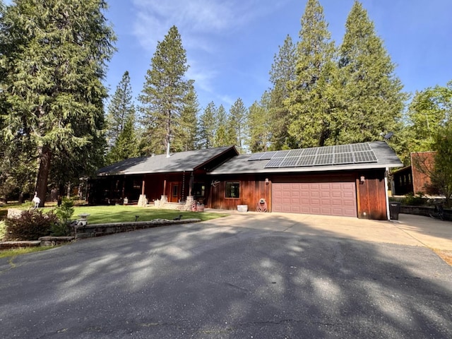 view of front of property with covered porch, a front yard, a garage, roof mounted solar panels, and aphalt driveway
