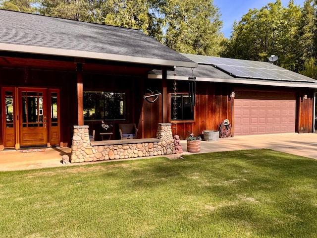 view of front of property with roof mounted solar panels, roof with shingles, a front lawn, and a garage