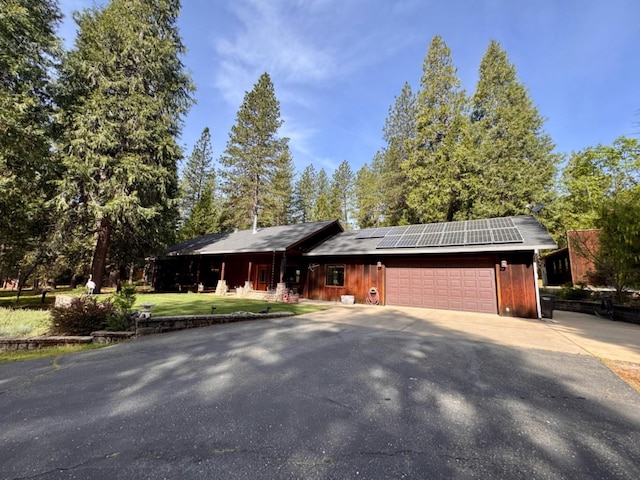 ranch-style house with roof mounted solar panels, an attached garage, and driveway