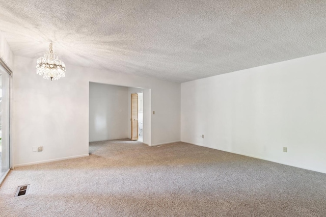 carpeted spare room with visible vents, a textured ceiling, and a notable chandelier