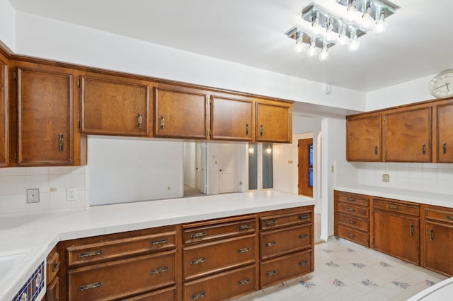 kitchen with light countertops, light floors, brown cabinetry, and backsplash