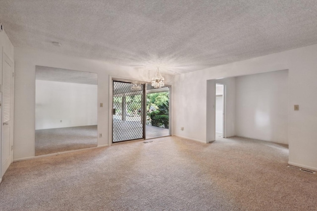 carpeted empty room featuring a textured ceiling and a notable chandelier