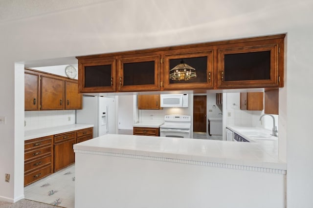 kitchen featuring white appliances, backsplash, a sink, and a peninsula