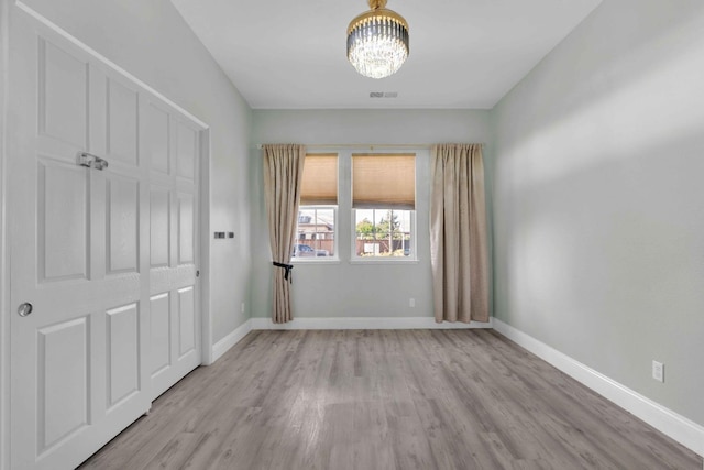 unfurnished bedroom with an inviting chandelier, light wood-style flooring, and baseboards