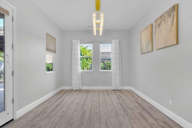 unfurnished dining area featuring baseboards, an inviting chandelier, and wood finished floors