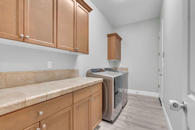 laundry room featuring light wood-style floors, baseboards, cabinet space, and washing machine and dryer