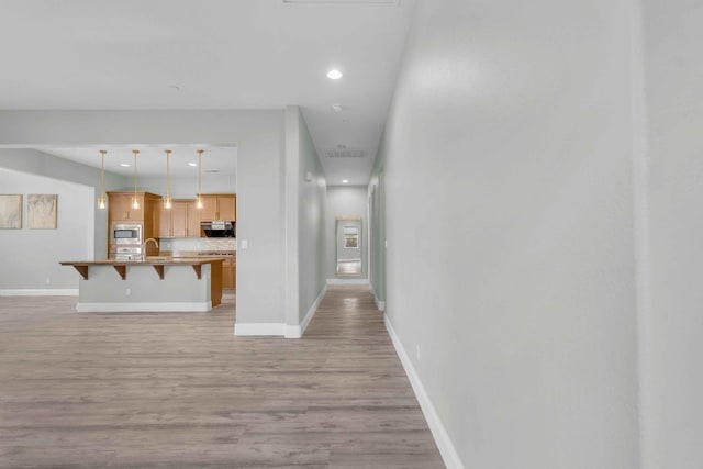 interior space featuring visible vents, baseboards, a breakfast bar area, light wood-type flooring, and stainless steel microwave