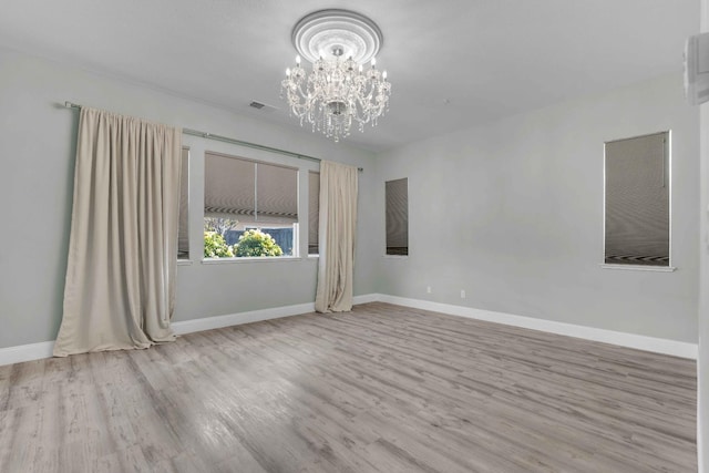 unfurnished room featuring baseboards, visible vents, wood finished floors, and a notable chandelier
