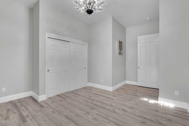 unfurnished bedroom featuring baseboards, an inviting chandelier, wood finished floors, and a closet