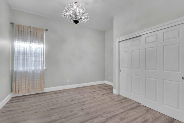 unfurnished bedroom featuring baseboards, wood finished floors, a notable chandelier, and a closet