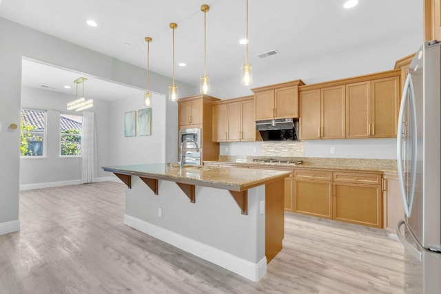 kitchen with light stone countertops, light wood-type flooring, under cabinet range hood, a breakfast bar, and stainless steel appliances