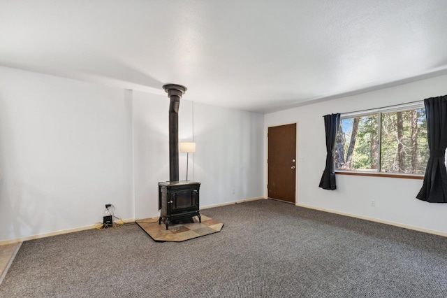unfurnished living room with baseboards, a wood stove, and carpet flooring