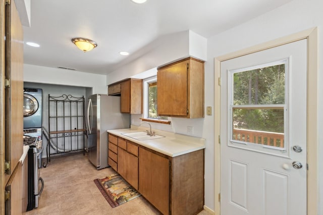 kitchen with a sink, light countertops, stacked washing maching and dryer, brown cabinetry, and freestanding refrigerator