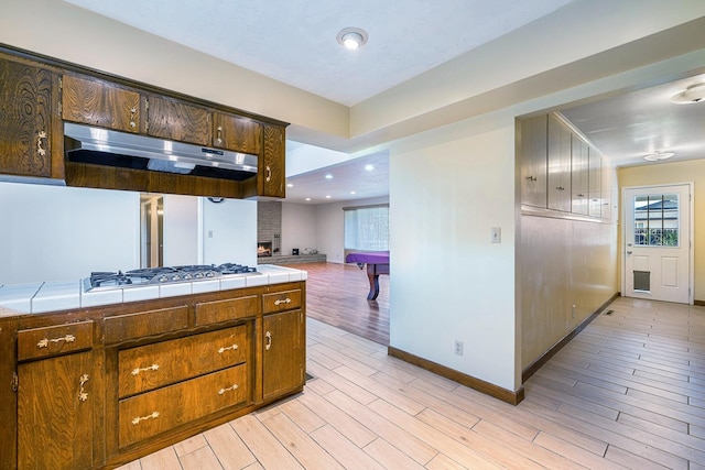 6154 E Alta Ave, Fresno, CA 93727 - kitchen with light wood finished floors, tile counters, baseboards, stainless steel gas stovetop, and under cabinet range hood