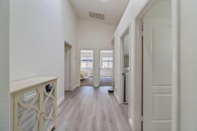 corridor with visible vents, baseboards, washer / dryer, a textured wall, and light wood-style flooring