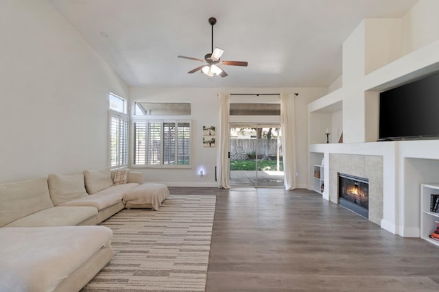 living room with a tiled fireplace, a ceiling fan, baseboards, and wood finished floors