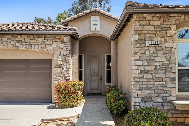 5534 N La Ventana Ave, Fresno, CA 93723 - view of exterior entry featuring driveway, a tile roof, a garage, stone siding, and stucco siding