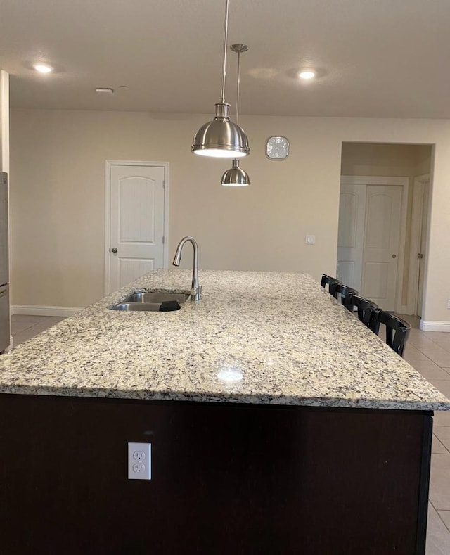 5244 W Fern Ave, Fresno, CA 93722 - kitchen featuring light stone countertops, hanging light fixtures, a sink, an island with sink, and light tile patterned floors