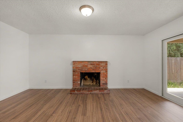 unfurnished living room with baseboards, a textured ceiling, a brick fireplace, and wood finished floors