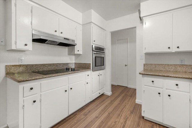 kitchen with wood finished floors, black electric cooktop, under cabinet range hood, white cabinetry, and oven